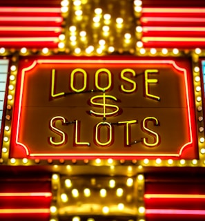 Bright neon lights display the words 'Loose Slots' with a dollar sign in the center. The sign is outlined with bulbs, creating a vibrant and flashy effect typical of a casino or entertainment venue.
