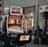 A collection of slot machines is situated inside a building with bright, colorful screens displaying various games and gaming themes. A person is seated nearby, seemingly relaxed with luggage beside them, and the atmosphere is lively with electronic displays.